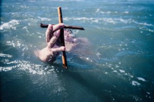 person drowning holding brown wooden cross above water at daytime